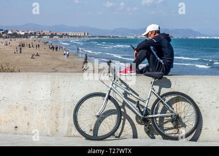 Il biker fa una pausa per la comunicazione mobile, Malvarrosa spiaggia sfondo, Valencia spiaggia Spagna vista mare Foto Stock