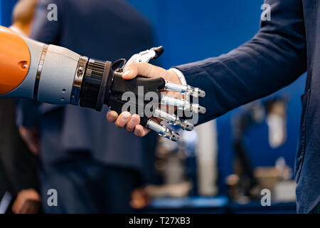 La mano di un uomo d'affari che stringono le mani con un robot androide. Il concetto di interazione umana con intelligenza artificiale. Foto Stock