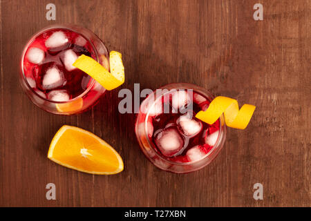 Due cocktail vivaci con Campari e orange curl contorni, con una fettina di arancio, girato da sopra al buio su un rustico sfondo di legno Foto Stock