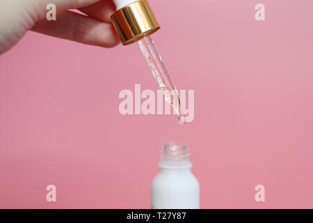 Pipetta con liquido in cui le particelle di oro sono visibili. Siero con particelle di oro per la pelle. Femmina lato tenendo un bellissimo dropper con liquido. Foto Stock