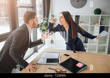 Sostengono tra il giovane uomo e donna. Lei urla e lotta con guy. Essi stare in camera a tavola. Materiali giacente sulla scrivania Foto Stock