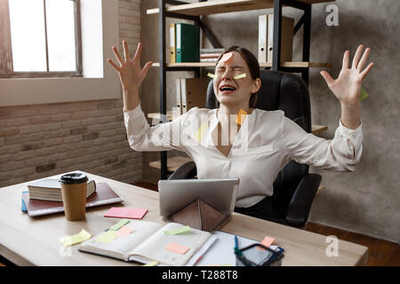 Giovane imprenditrice hanno attacco di panico dal multitasking. Ha un sacco di lavoro. Modello preoccupare. Ella ha hysterics. Seduta a tavola in camera. Foto Stock