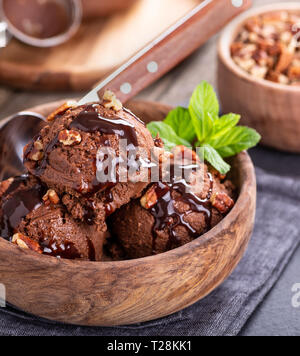 Vista dettagliata del gelato al cioccolato con le noci pecan e la salsa in un recipiente di legno Foto Stock