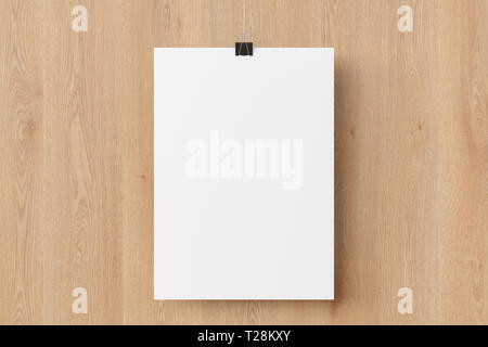 Poster di carta bianca appeso a una clip per rilegatura sullo sfondo di una parete di legno Foto Stock