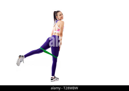 Una donna ypung coach in sportivo viola corto superiore e palestra leggings rende balzi in avanti con i piedi avanti con lo sport fitness bande di gomma, allungare le gambe su Foto Stock