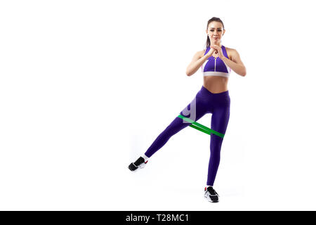 Una donna ypung coach in sportivo viola corto superiore e palestra leggings rende balzi in avanti con i piedi avanti con lo sport fitness bande di gomma, allungare le gambe su Foto Stock