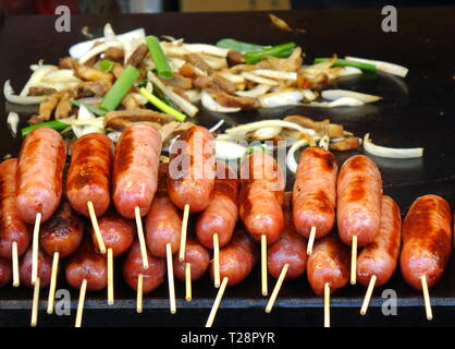 Un venditore ambulante arrosti freschi salsicce e patate fritte di maiale e perdite Foto Stock