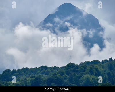 Alta montagna con verdi pendii nascosti nelle nubi e nebbia. Nero montagna piramidale, Krasnaya Polyana, Sochi, Caucaso, Russia. Foto Stock