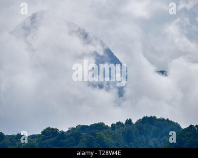Alta montagna con verdi pendii nascosti nelle nubi e nebbia. Nero montagna piramidale, Krasnaya Polyana, Sochi, Caucaso, Russia. Foto Stock