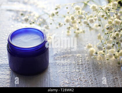 Blu di un vasetto di vetro con fatti in casa deo organico bianco sullo sfondo di legno con piccoli fiori bianchi e lo spazio per la copia. Prodotti per la cura della pelle del concetto. Foto Stock