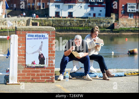 Paio mangiare Fish & Chips seduta sul porto di Whitby , a nord della Costa dello Yorkshire, Inghilterra, Regno Unito, GB. Foto Stock