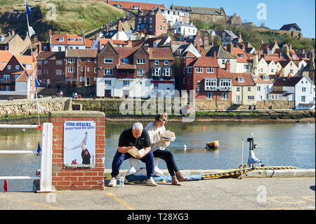 Paio mangiare Fish & Chips seduta sul porto di Whitby , a nord della Costa dello Yorkshire, Inghilterra, Regno Unito, GB. Foto Stock