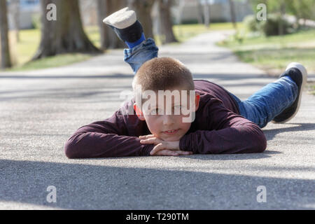 Grazioso fanciullo, biondo toddler boy giocando all'esterno giacente in corrispondenza di strada Foto Stock