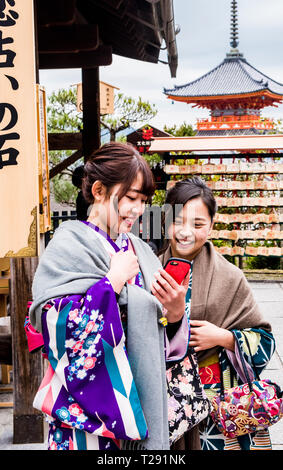 Due donne in abito tradizionale, guardando smartphone, sorridente, Kiyomizu-dera tempio, Kyoto, Giappone Foto Stock