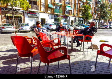 Tre uomini siedono fuori dal bar e bevono birra in bottiglia, il bar di Valencia Street Quart de Poblet, quartiere di Valencia, Spagna Foto Stock