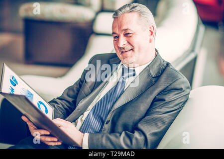 Finanziere esperto con i grafici finanziari seduto in poltrona Foto Stock