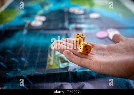 La mano lanci di dadi di colore giallo sul campo di gioco. Buona fortuna e le emozioni. Giochi da tavolo. Momenti di gioco nella dinamica Foto Stock