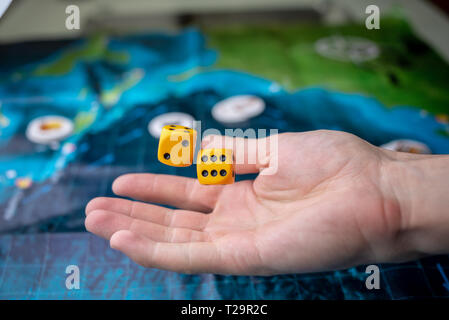 La mano lanci di dadi di colore giallo sul campo di gioco. Buona fortuna e le emozioni. Giochi da tavolo. Momenti di gioco nella dinamica Foto Stock