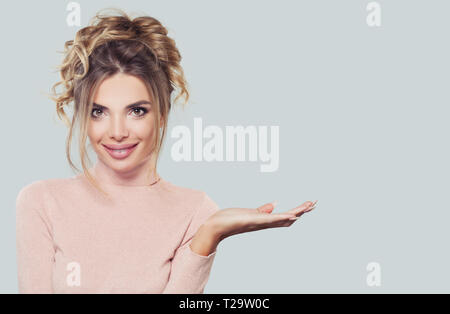 Modello sorridente donna mostra vuoto mano aperta su sfondo bianco. Bella ragazza con pelle chiara, Updo capelli e specchio Foto Stock