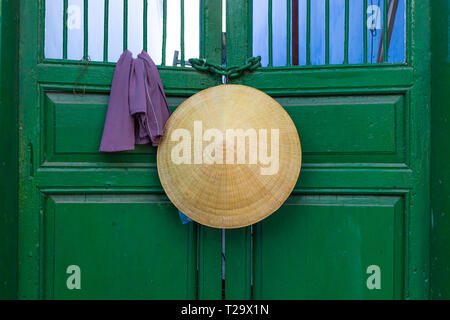 In stile asiatico cappello conico appeso su una porta verde in Vietnam . Foto Stock