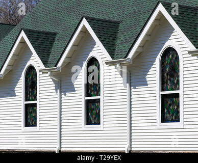 Obliqua di vista esterna di color verde scuro e tetto bianco luminoso con parete della chiesa, con tre tetto triangolare gables al di sopra di tre finestre di vetro colorato Foto Stock