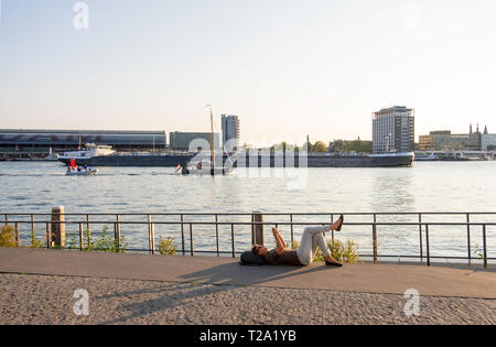 Amsterdam, Paesi Bassi - 02 Settembre 2018: Donna appoggiata sul fiume Amstel shore contro lo sfondo del porto e la stazione centrale di Amsterdam Foto Stock