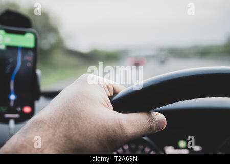 Google maps su un telefono intelligente attaccata al supporto sul windsceen di una vettura - visto dal conducente - con una vista delle mani sul volante. Foto Stock