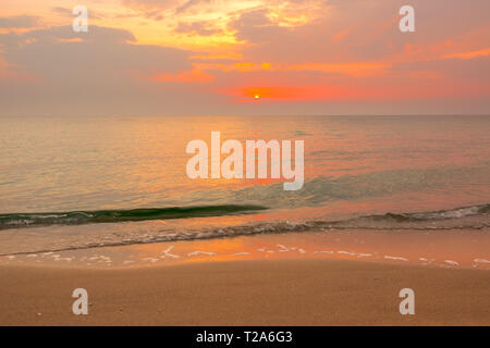 Arancione tramonto sul mare calmo. Onda Verde viene eseguito su di una spiaggia di sabbia Foto Stock