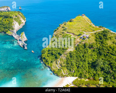 Indonesia. Costa rocciosa di un'isola tropicale. Acque turchesi e una piccola spiaggia. Numerosi rifugi sulla cima della scogliera e una scala lungo il pendio. Foto Stock