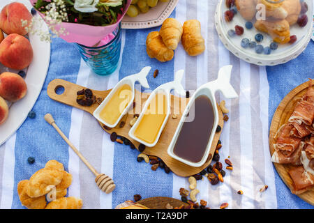 Set di tre sauceboats bianco con il dolce miele sul vassoio in legno a picnic food lay out dello sfondo. Foto Stock