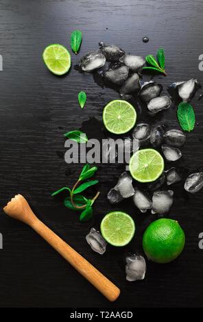 Limes, foglie di menta e i cubetti di ghiaccio su sfondo nero. Ingredienti per cocktail mojito. Vista dall'alto. Foto Stock