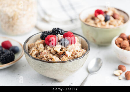 Una sana colazione a base di cereali porridge con frutti di bosco e i dadi nel recipiente. Primo piano. Foto Stock