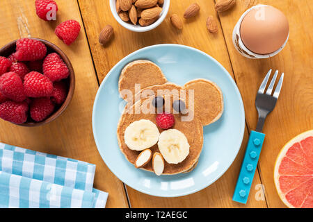 Colazione colorata per i bambini. Funny pancake arte cibo, uova sode e frutta su un tavolo di legno Foto Stock