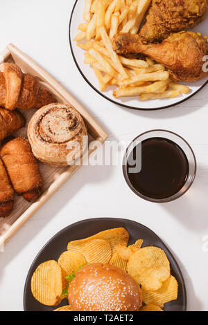 Pane appena sfornato, panini, grandi hamburger, fritto croccante di pollo e patatine fritte sul tavolo bianco - cibo malsano concetto Foto Stock