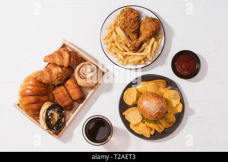 Pane appena sfornato, panini, grandi hamburger, fritto croccante di pollo e patatine fritte sul tavolo bianco - cibo malsano concetto Foto Stock