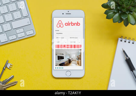 Un iPhone che mostra il sito web Airbnb poggia su uno sfondo giallo tabella con una tastiera, tasti, blocco note e di impianto (solo uso editoriale). Foto Stock