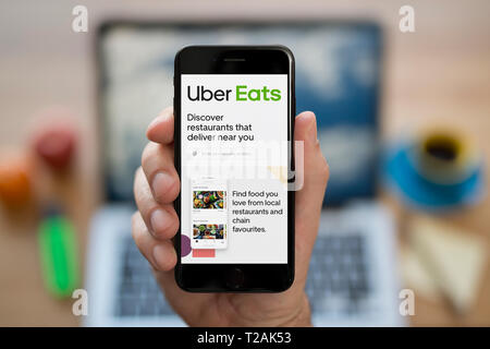 Un uomo guarda al suo iPhone che visualizza la Uber mangia logo (solo uso editoriale). Foto Stock