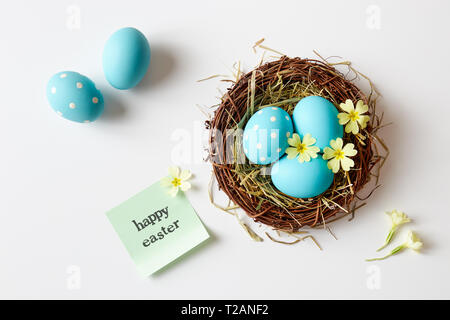 Decorazione di pasqua con nido, uova e fiori di primavera. Blue uova di Pasqua nel nido con 'Felice Pasqua messaggio". Foto Stock
