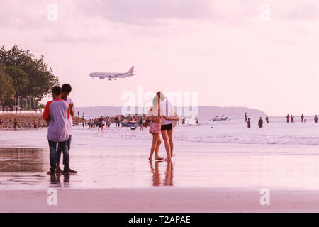 Bali, Denpasar, 2018-04-07: aereo dal Qatar airlines vola sopra il mare spiaggia al tramonto. Aeromobile è lo sbarco su l'acqua oceanica e turisti. Foto Stock