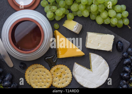 Scheda formaggio di formaggio cheddar, camembert, uva, cracker e miele close up - vista superiore Foto Stock