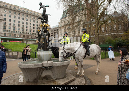 LONDON, Regno Unito - 22 Marzo 2019: poliziotta dalla Polizia Metropolitana di ramo montato in attesa mentre i loro cavalli di bere acqua da una fontana pubblica Foto Stock