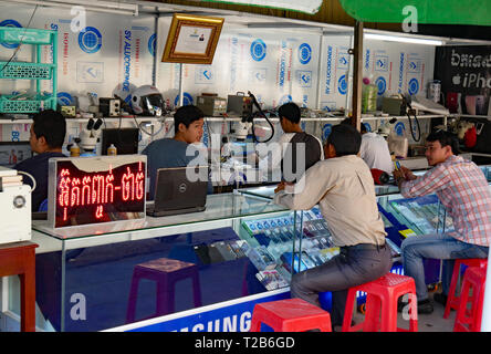 Battambang, Cambogia. Un telefono cellulare repair shop in un cambogiano città mercato. Un cliente descrive un problema con un tecnico 15-12-2018 Foto Stock