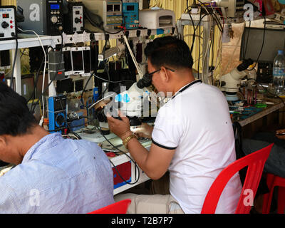 I tecnici di riparazione telefoni mobili in un aperto fronteggiata shop in un cambogiano città mercato. Battambang, Cambogia 13-12-2018 Foto Stock
