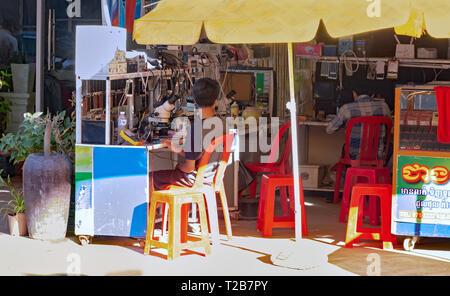 I tecnici di riparazione telefoni mobili su strada in un aperto fronteggiata shop in un cambogiano città mercato. Battambang, Cambogia, 15-12-2018 Foto Stock