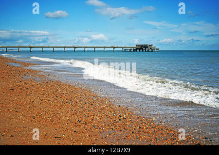 Mare di scena a trattare in Kent England con le onde provenienti sulla spiaggia di ciottoli e il molo che si allunga nel mare blu acqua con un cielo nuvoloso sopra Foto Stock