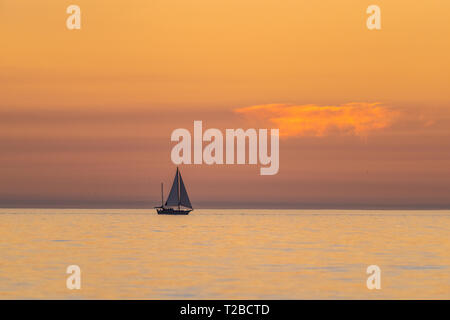 Una imbarcazione a vela è visto da Fort Myers Beach, Florida contro la barca a vela al tramonto di sera i colori del tramonto e nuvole sottili sull'oceano aperto. Foto Stock