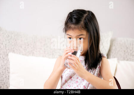 Carino bambina acqua potabile sul divano di casa. health care concetto. Foto Stock