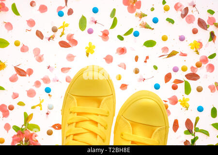 Sneakers giallo sulla colorata primavera superficie decorata, vista dall'alto lay piatto Foto Stock