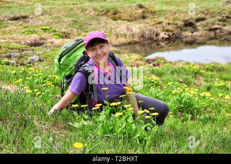 Donna sorridente si siede sul fiore prato alpino. Viaggio estivo lungo la tundra di montagna in Siberia Orientale. Attività per il tempo libero in mezzo alla natura Foto Stock