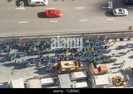 Arial vista di un grande gruppo di lavoratori edili, raggruppati sul lato della strada durante un drill incendio Foto Stock